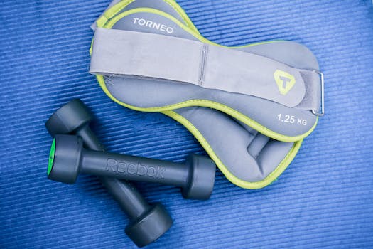 From above of modern dumbbells and leg weight belts placed on blue fitness mat in studio