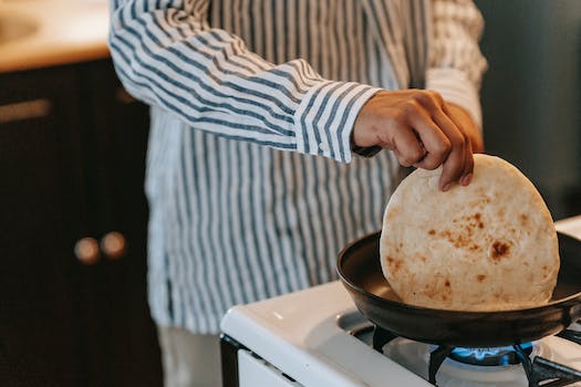Crop unrecognizable male in striped shirt touching pancake on cooker of modern kitchen on blurred background