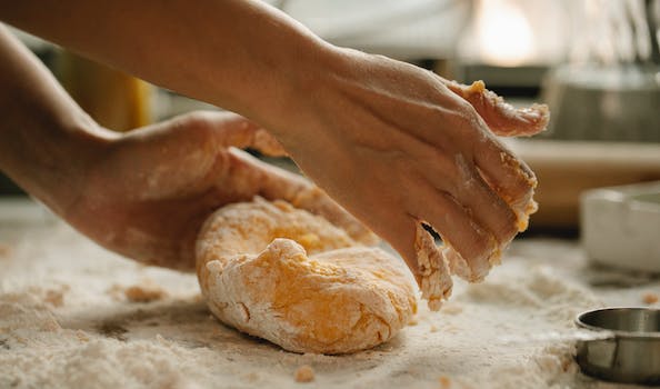 Unrecognizable woman kneading fresh dough on wooden table with flour while preparing food in kitchen
