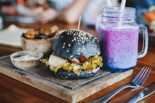 Delicious hamburger and mug of cold smoothie on wooden board