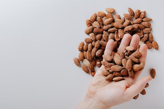 From above of anonymous male taking tasty organic almonds from pile of nuts placed on white background isolated illustrating healthy food concept