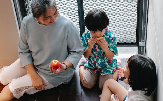 Adorable ethnic siblings eating fruits with grandmother at home