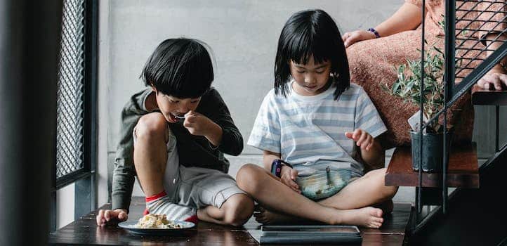 Asian children watching video on tablet and having snack at home
