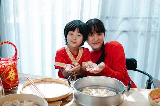Happy Asian teenage girl with dark hair cuddling with little brother and demonstrating traditional jiaozi dumplings during lunch preparation in kitchen