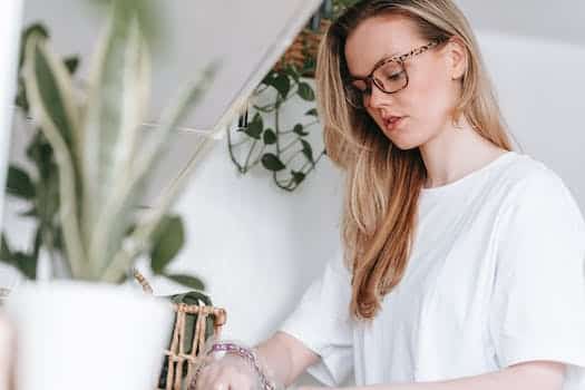 Low angle of focused female in eyeglasses and home t shirt standing at counter with green potted plants while cooking lunch snack at home