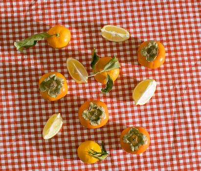 Top view of healthy food of lemon persimmon and tangerine placed on red checkered tablecloth