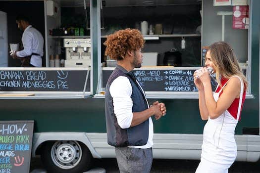 Young diverse couple eating takeaway sandwich while standing near food truck