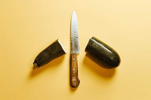 From above of fresh sliced zucchini placed on yellow background with sharp knife with wooden handle between halves of vegetable