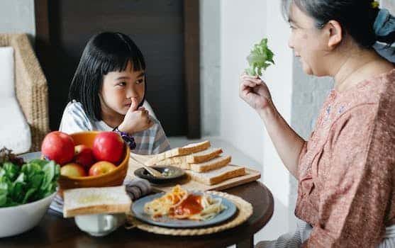 Smiling grandmother showing fresh leaf lettuce while sitting against cute Asian girl showing like gesture and looking at each other