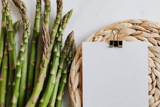 Top view of asparagus pods with sheets of paper fastened by paper clip on white desktop