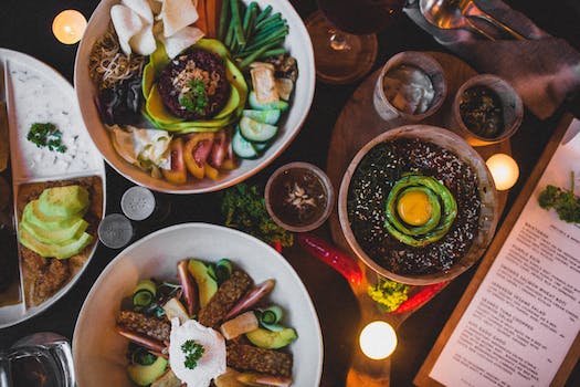 Top view of bowls with different salads with fresh vegetable slices and white sauce near bowl with lentils and egg yolk on top with menu and candles in cafe