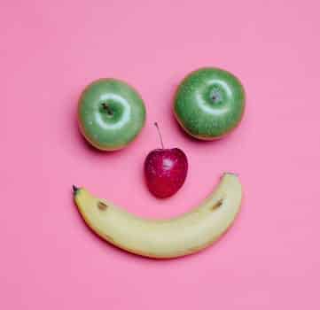 Top view of fresh ripe banana and green and red apples arranged as smile on pink background