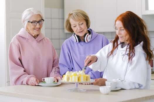 Cheerful woman cutting cake while drinking tea together with female friends
