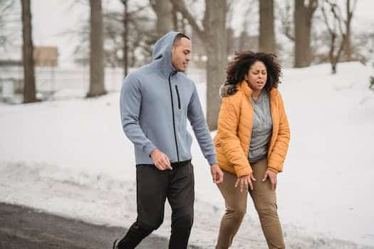 Exhausted plump African American female in outerwear with black personal instructor on pathway in snowy park during training in winter time