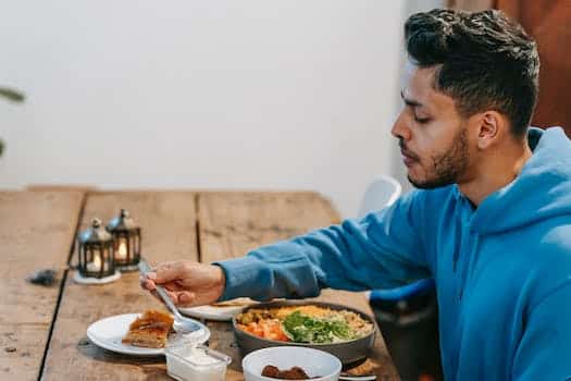 Side view of ethnic male in blue hoodie eating dessert and tasty meal at wooden table