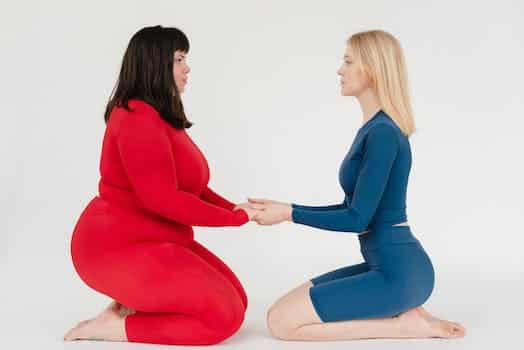 Full body side view of plus size woman and slender female instructor in activewear holding hands and looking at each other on white background