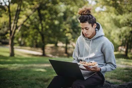 Young concentrated man surfing netbook while preparing for exams and eating pizza in park